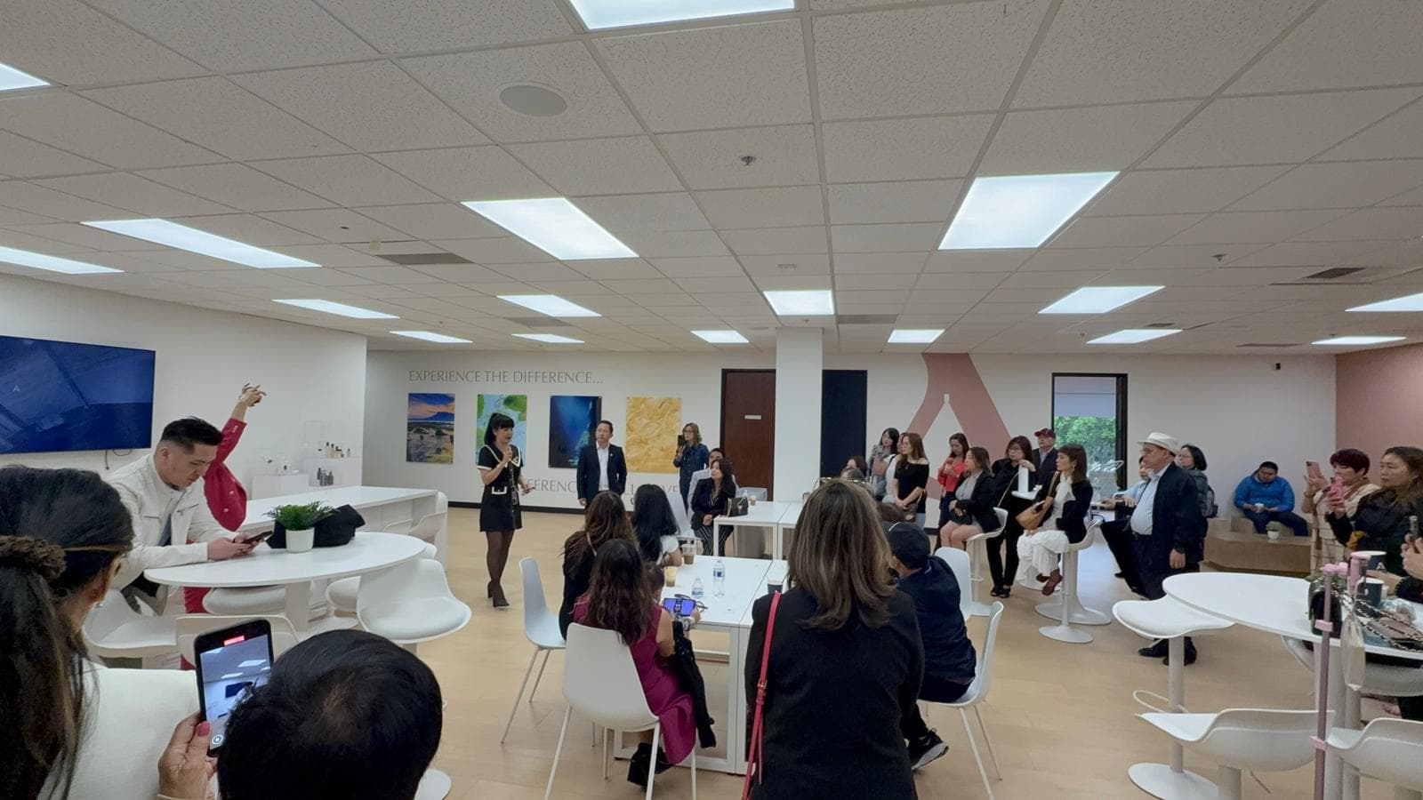 A speaker addressing attendees seated and standing in a bright presentation room.